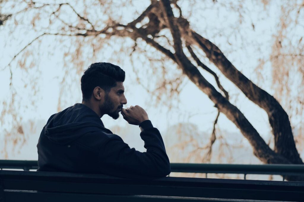 Aries Man in deep thought sitting on a bench in a serene autumn park setting.