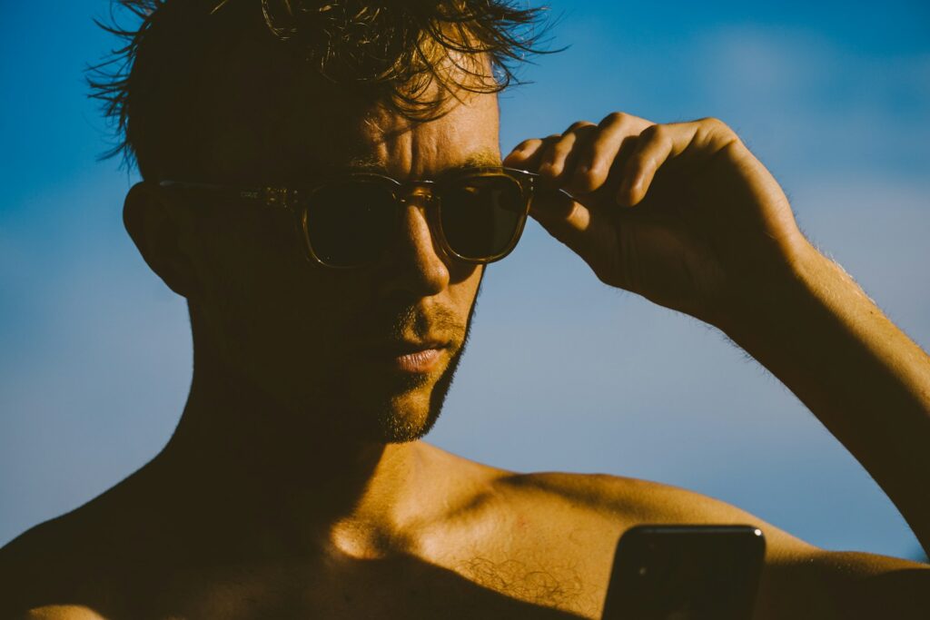 Sagittarius man wearing black sunglasses holding black smartphone during daytime